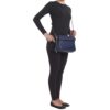A person wearing a black long-sleeve top, black pants, and black flats stands with the Clutch-Style Concealed Carry Purse with Shoulder Strap in Blue.