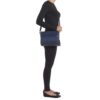 A person in black clothing stands in profile holding the Clutch-Style Concealed Carry Purse with Shoulder Strap in Blue, set against a plain white background.